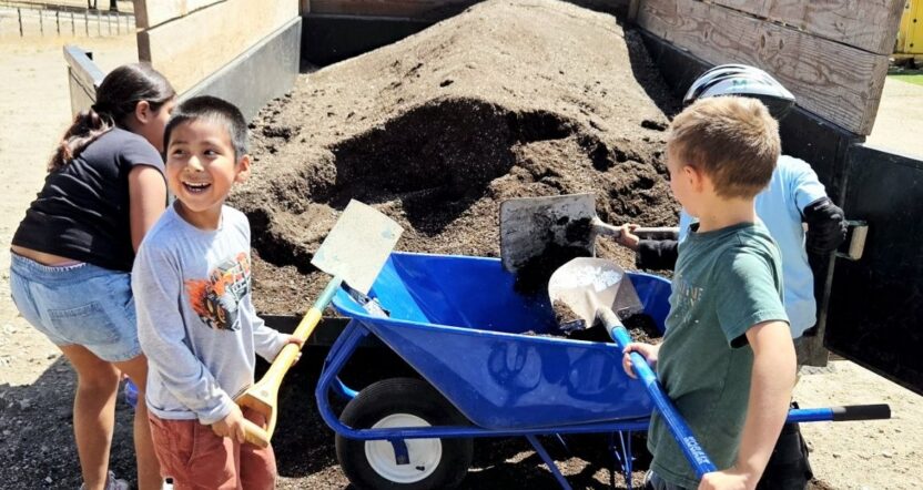 kids shoveling dirt into a wheel barrel and smiling
